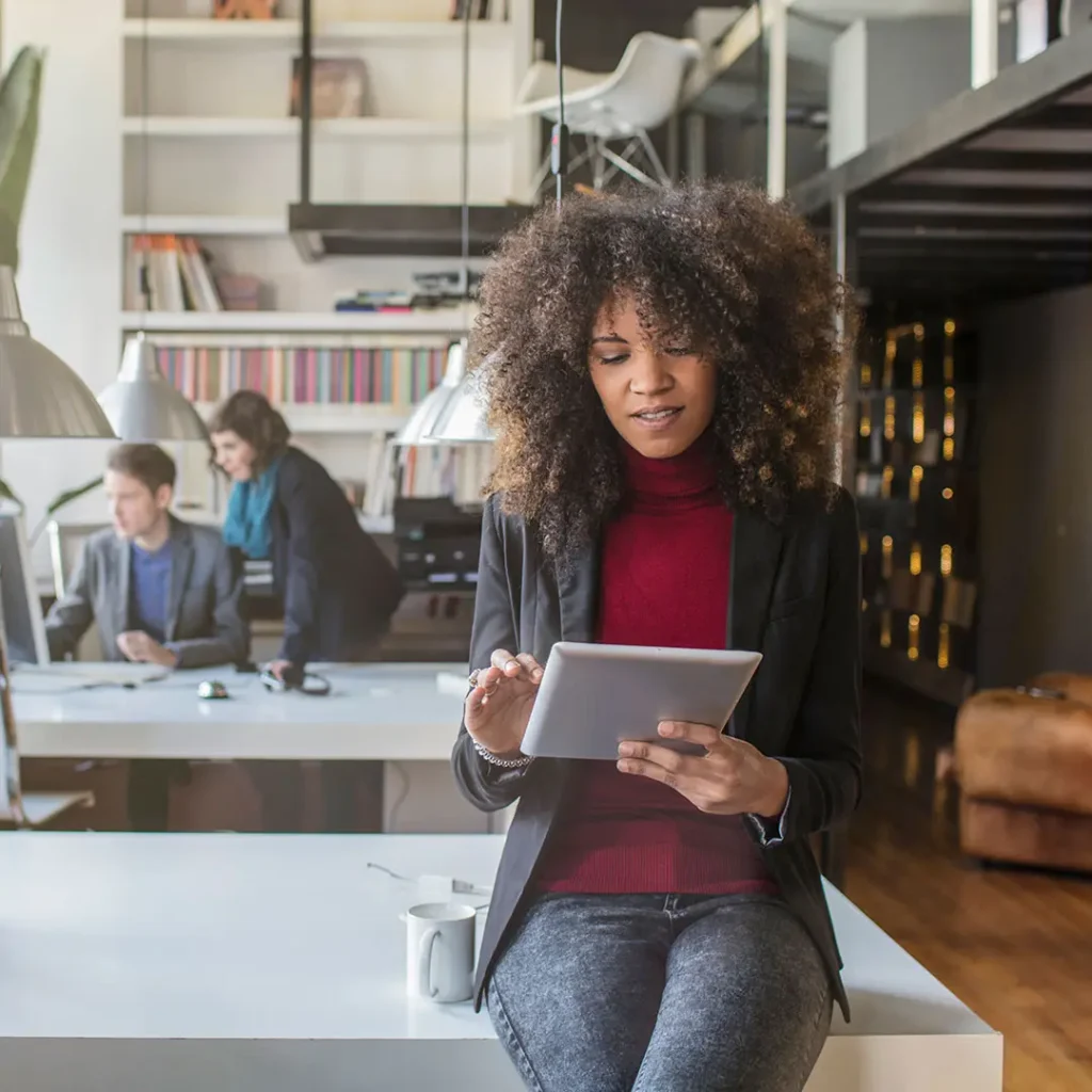 A professional woman using a tablet in a modern office, with colleagues working in the background, symbolizing teamwork and productivity.