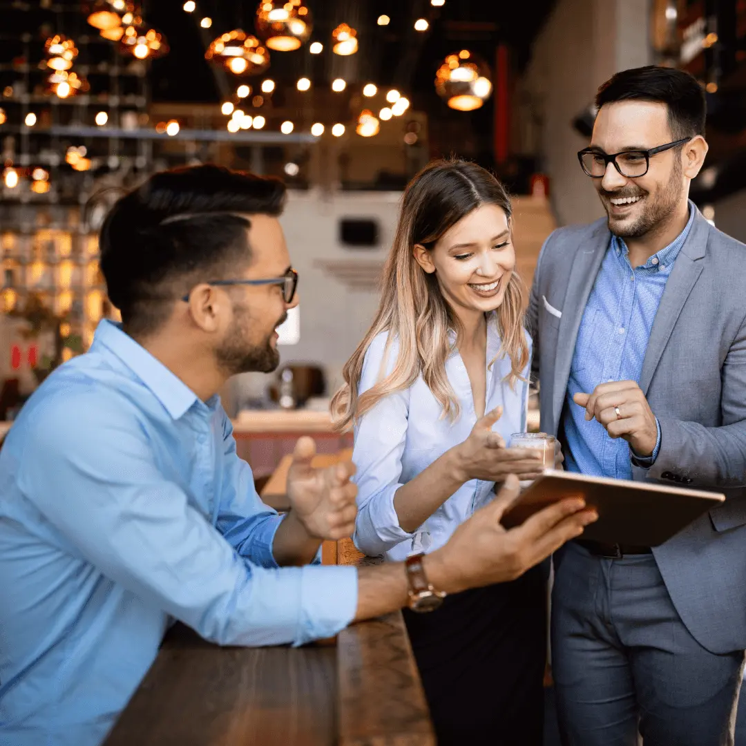 Three professionals smiling and discussing ideas while reviewing information on a digital tablet in a modern office setting.
