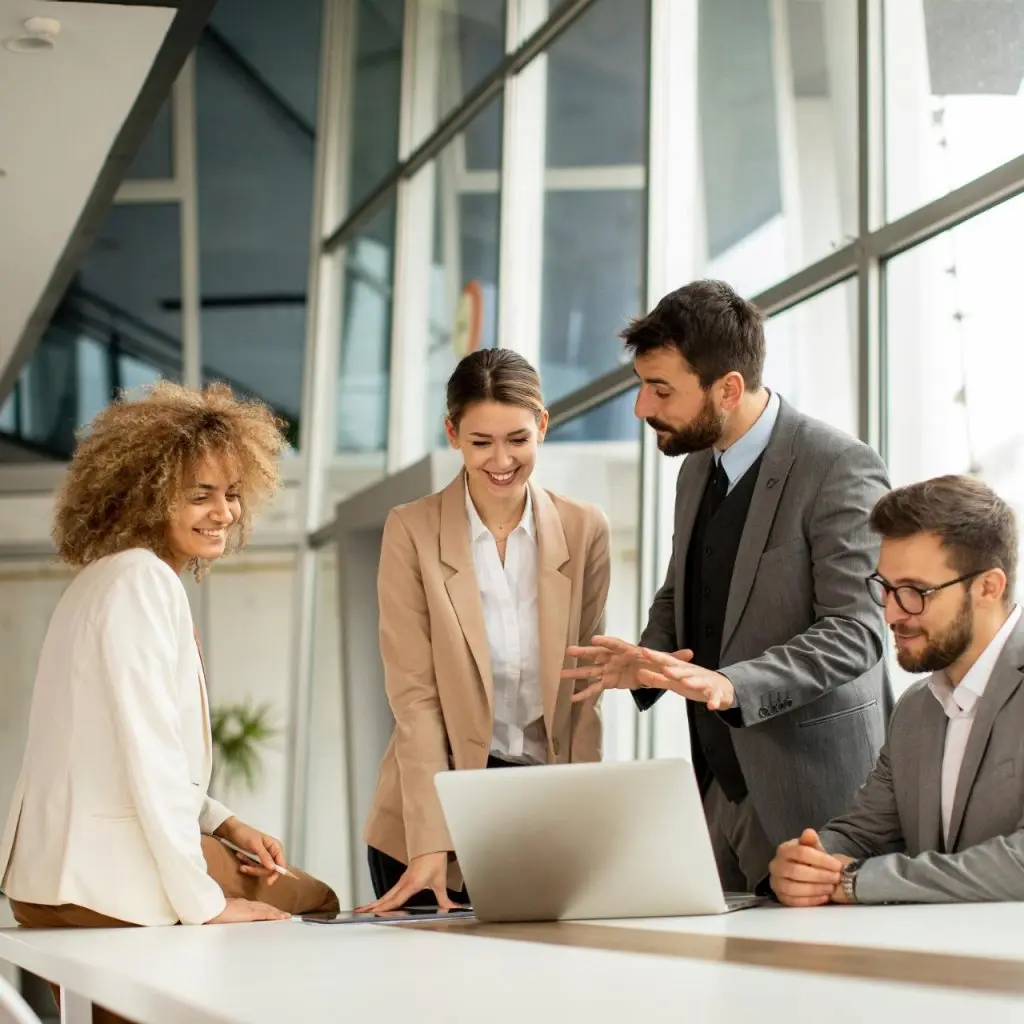 Group of business professionals discussing project ideas around a laptop in a modern office with large window