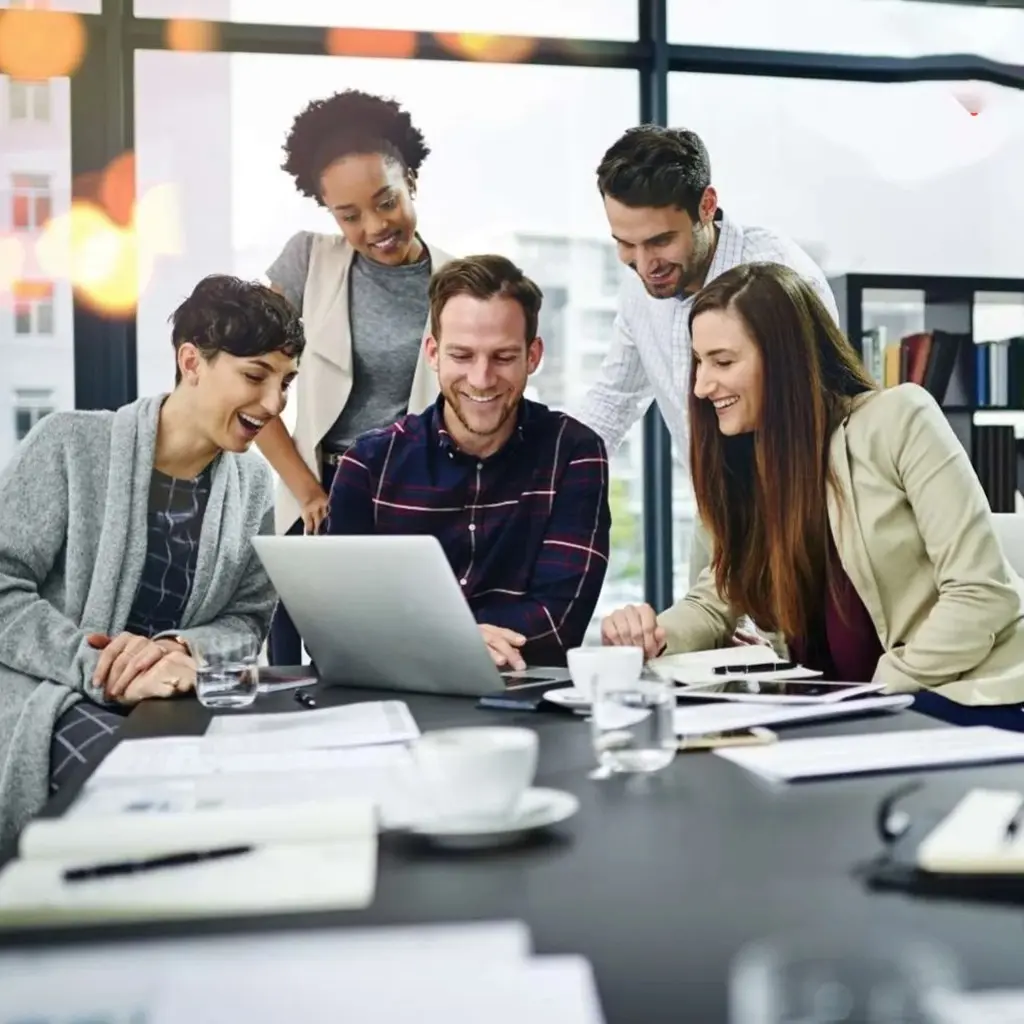 Group of professionals gathered around a laptop in a bright office, collaborating on a business project and sharing ideas