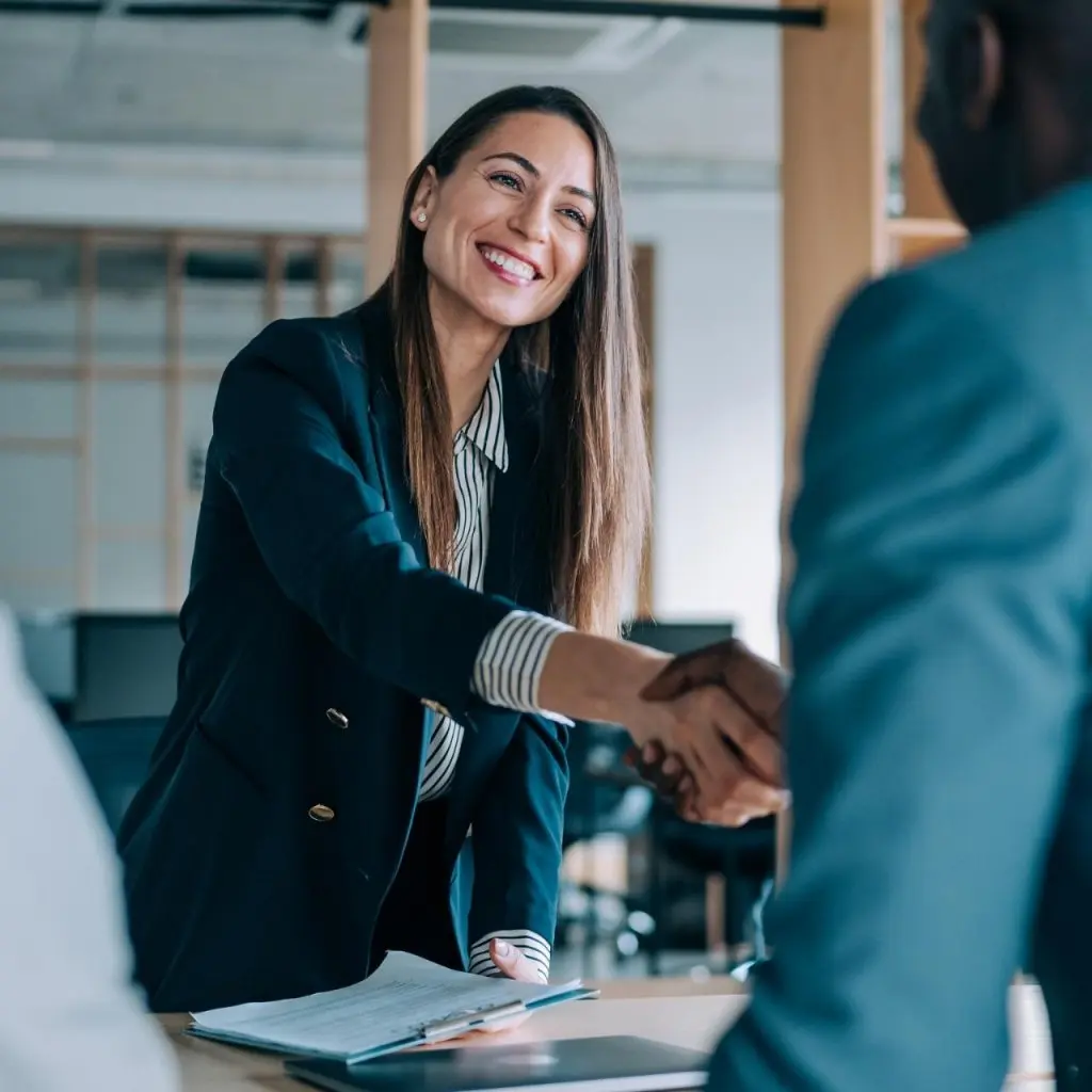 Smiling businesswoman in a meeting shaking hands with a colleague, showing successful partnership and professionalism