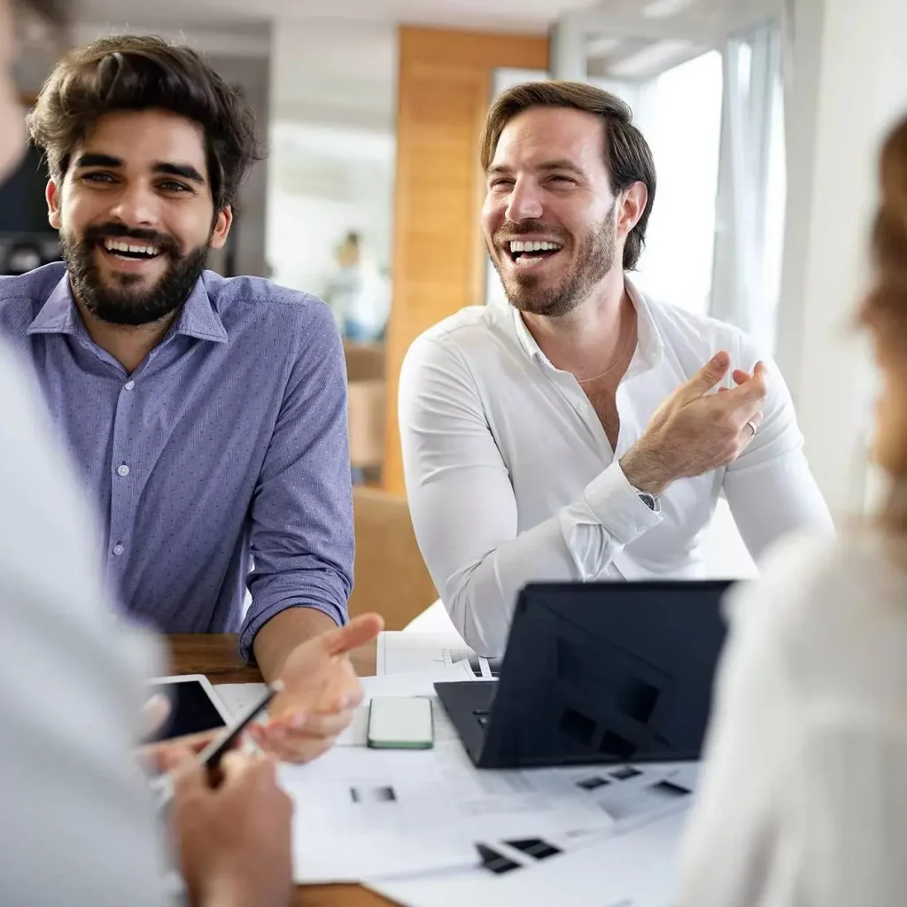 Smiling business professionals having a discussion around a table with laptops and documents in a bright modern office