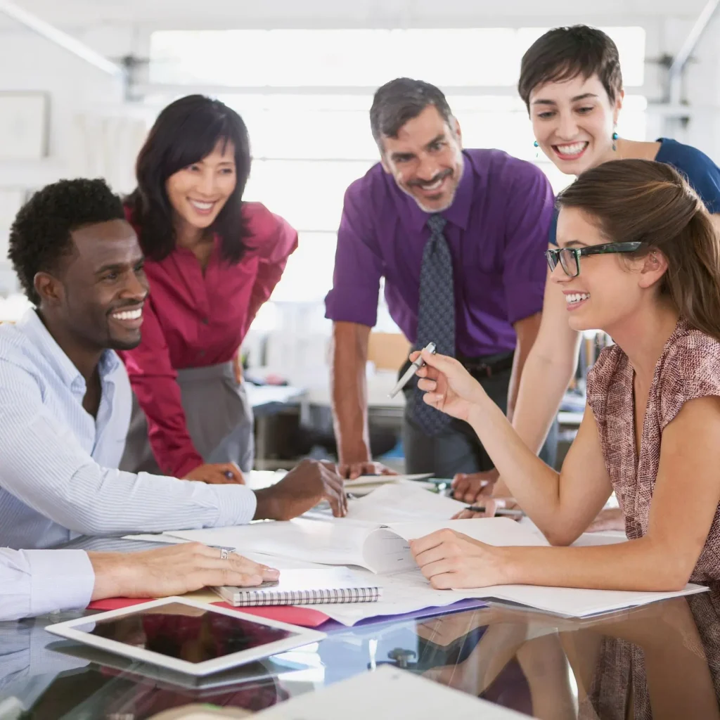 Smiling business team gathered around a desk in a bright office, collaborating and sharing ideas during a creative meeting