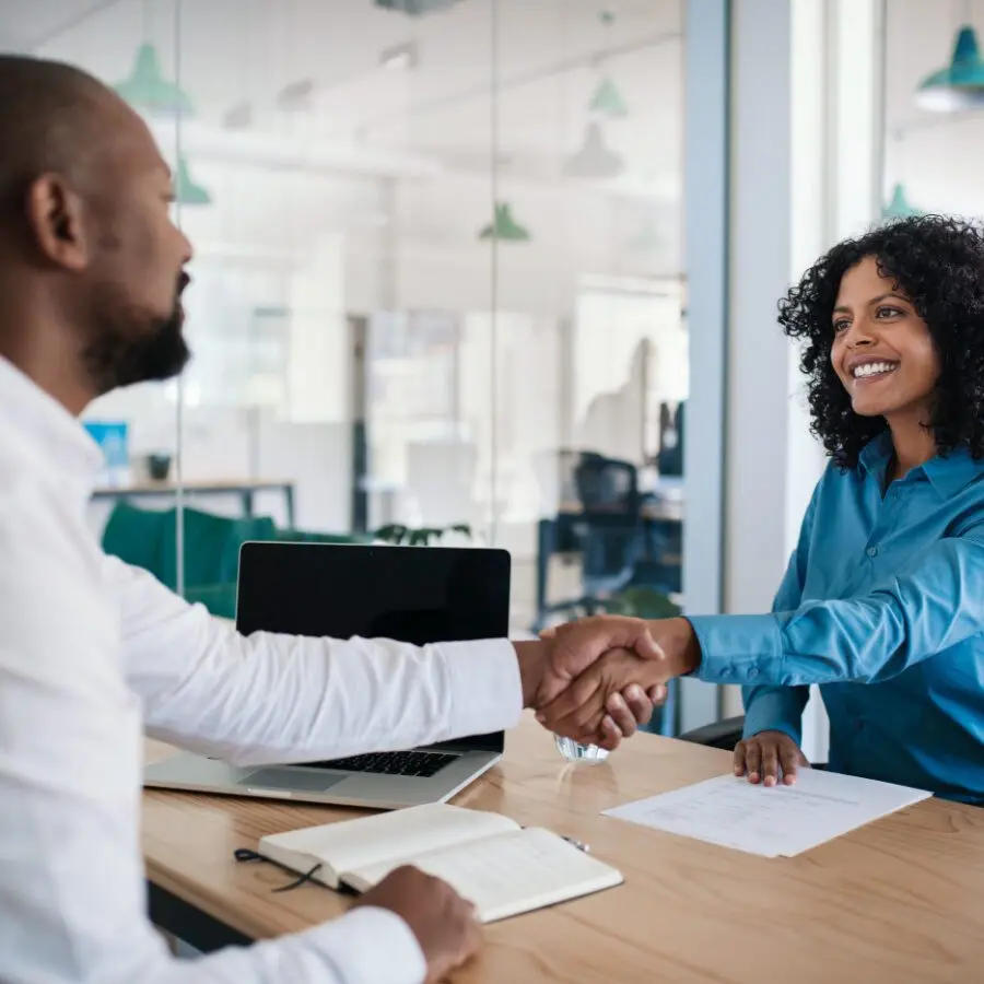 Two professionals shaking hands across a desk in a modern office, symbolizing agreement, partnership, or successful negotiation