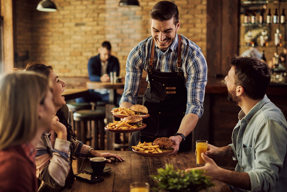 A smiling waiter serves burgers and fries to happy friends at a rustic restaurant, creating a warm and welcoming dining experience