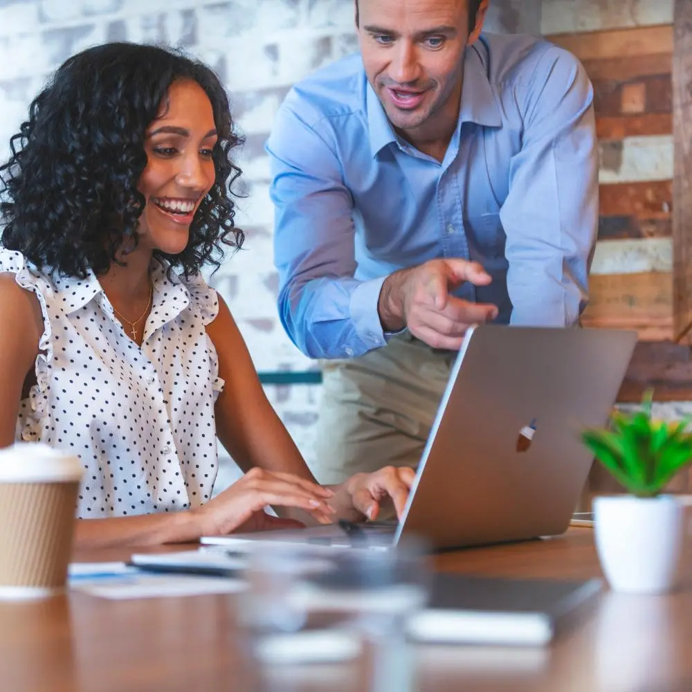 Two colleagues collaborating at a laptop in a modern office, smiling and discussing ideas during a productive meeting.